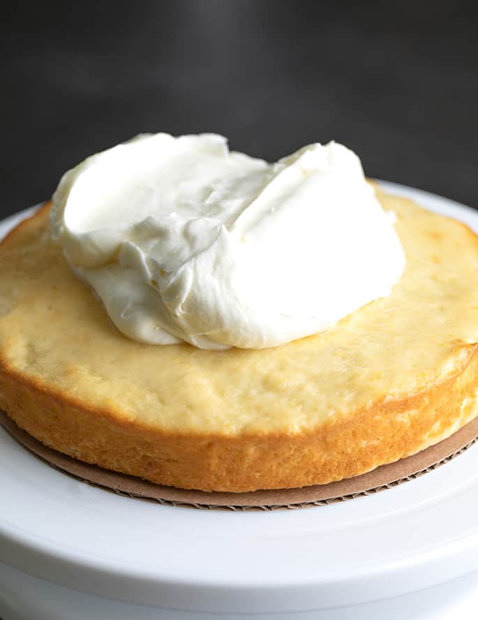 Round lemon cake with big dollop of white frosting on a white cake turner