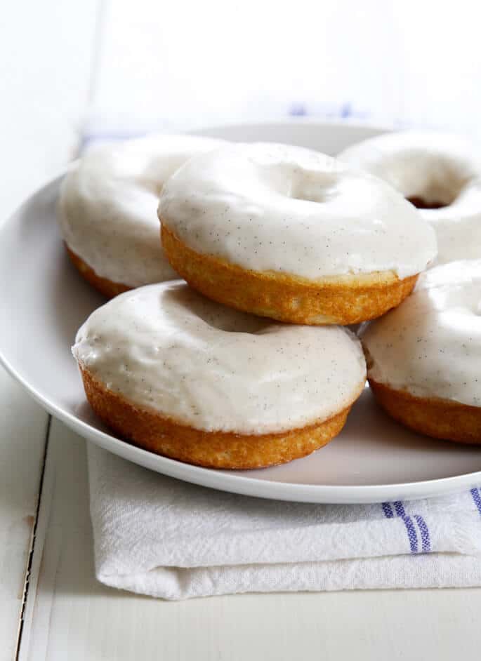 Vanilla cake donuts with white glaze stacked on a platter