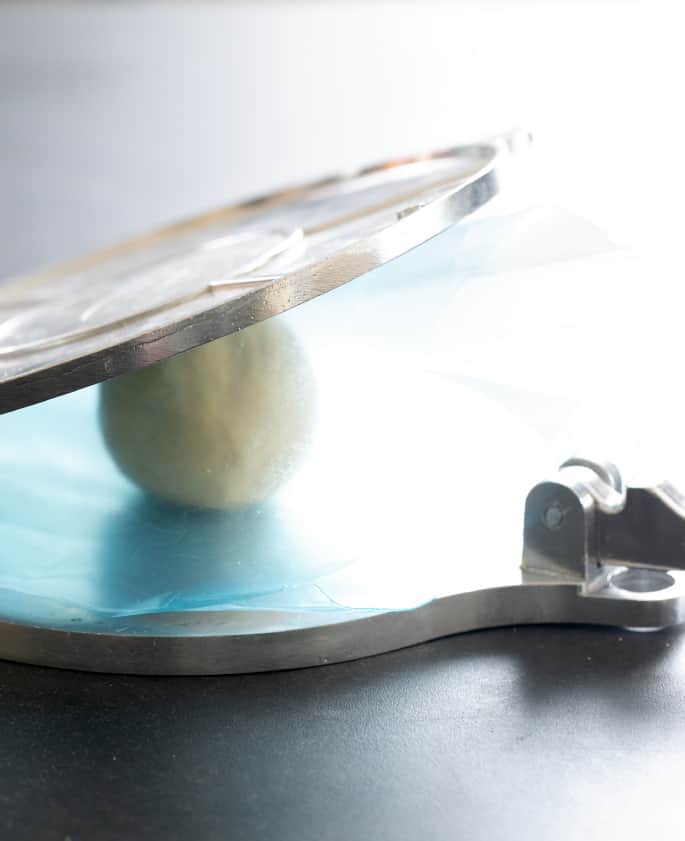 A ball of masa dough sitting in the middle of a tortilla press