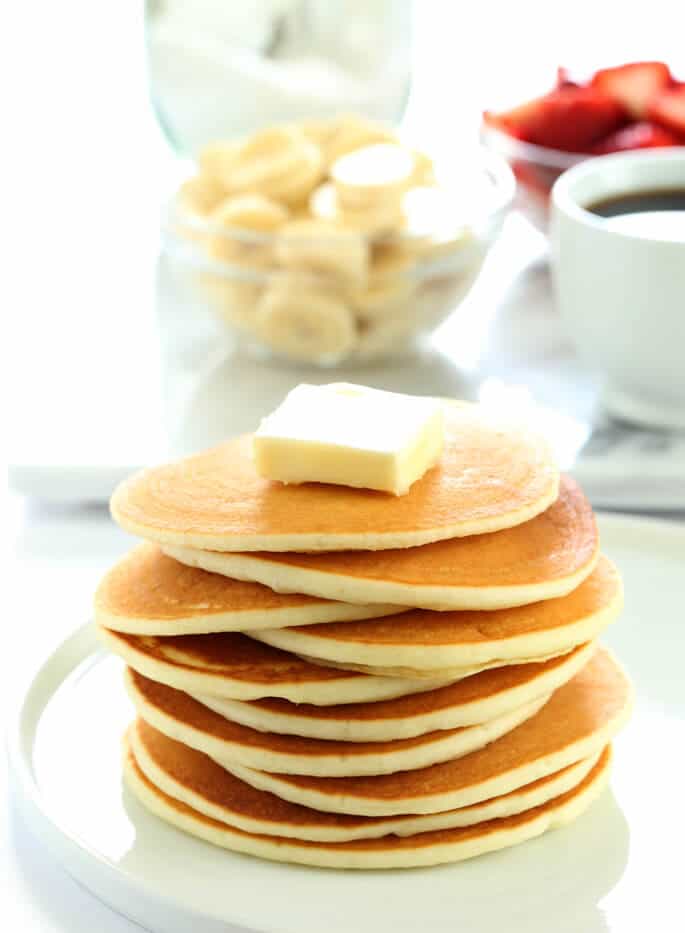 A tall stack of gluten free pancakes with a big pat of butter on top of the stack