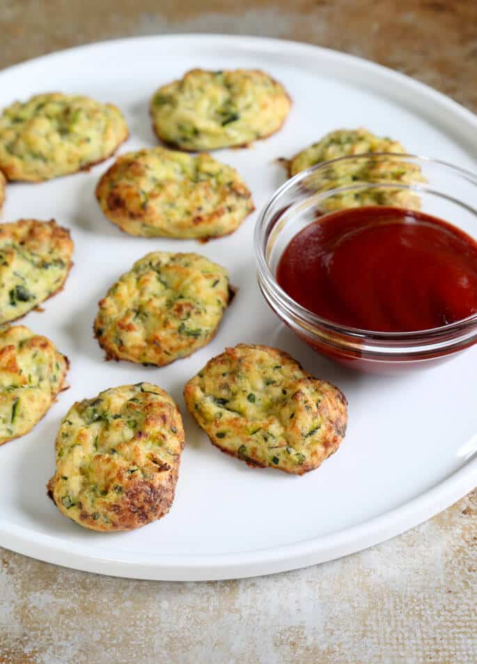 A white plate with red sauce and zucchini tots