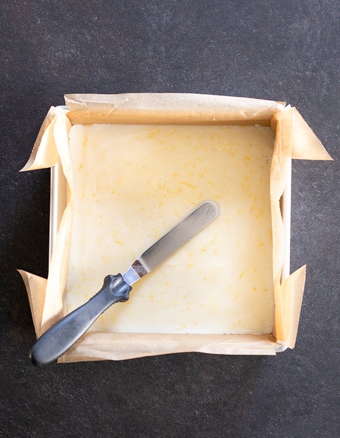 Overhead image of a square baking pan with raw crust and a spatula