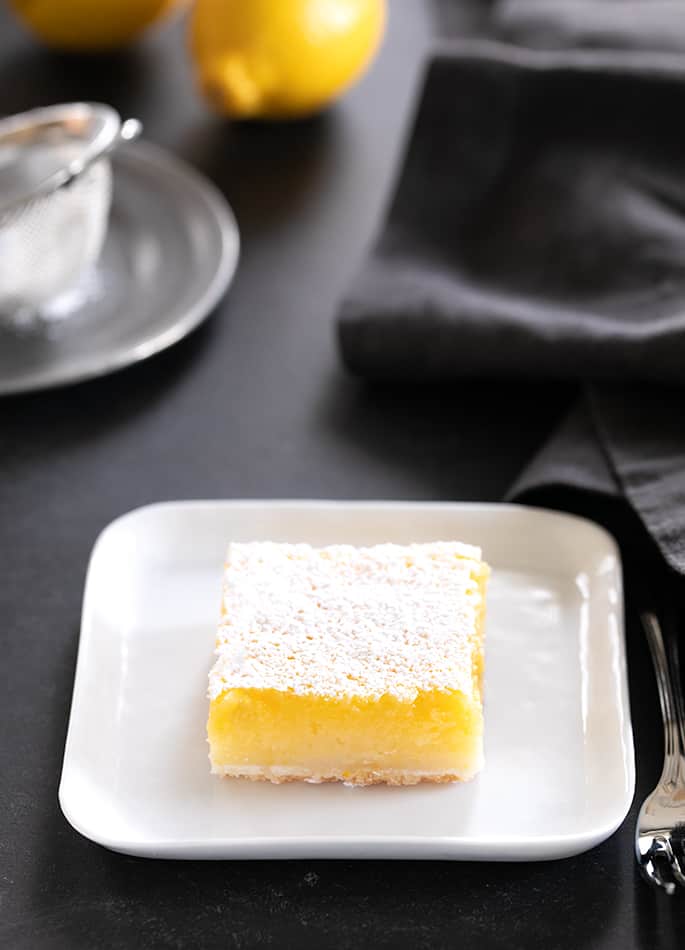 A single lemon bar on a small square plate