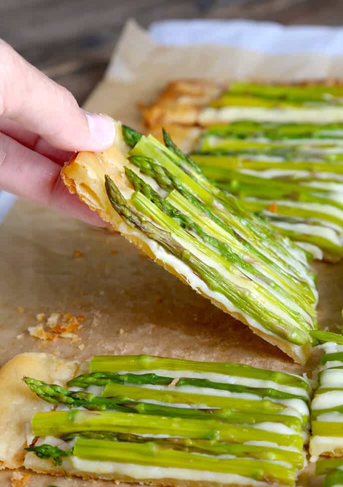 Piece of asparagus tart being picked up on parchment paper