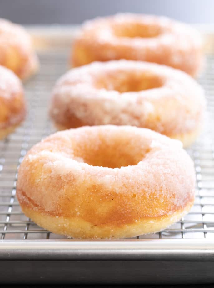 Vanilla cake donuts with a sugar glaze on a wire rack