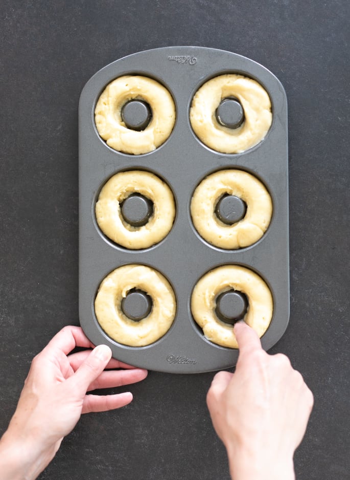 Overhead image of hands shaping vanilla cake donut dough in donut pan