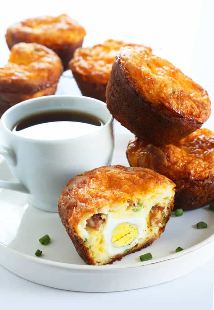 A close up the inside of a breakfast muffin with bacon and egg on a white plate with a cup of coffee 