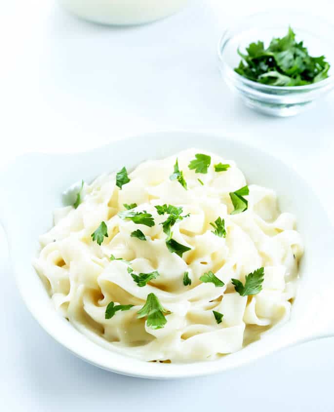 Noodles with Alfredo sauce and herbs on top in a white dish