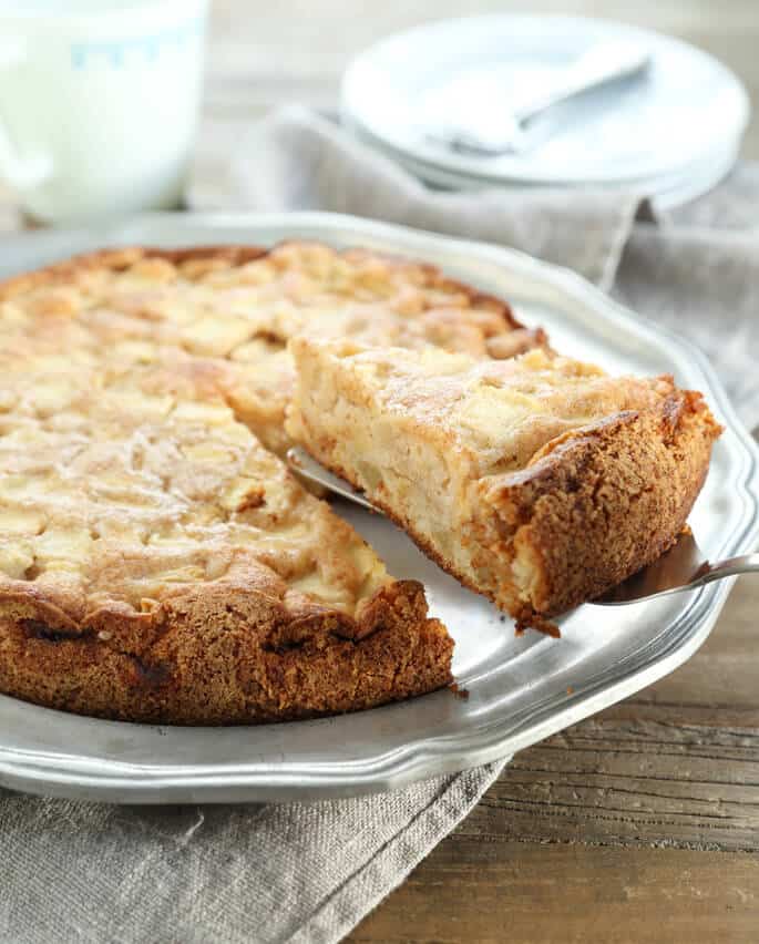 An apple cake on a silver surface with a slice being taken 