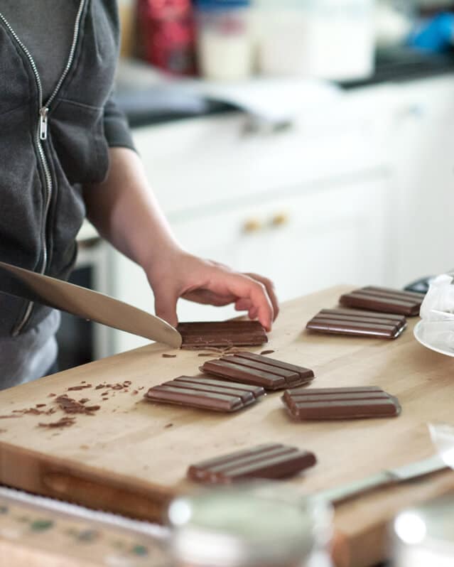 A person cutting \"kit Kat\" bars on a cutting board