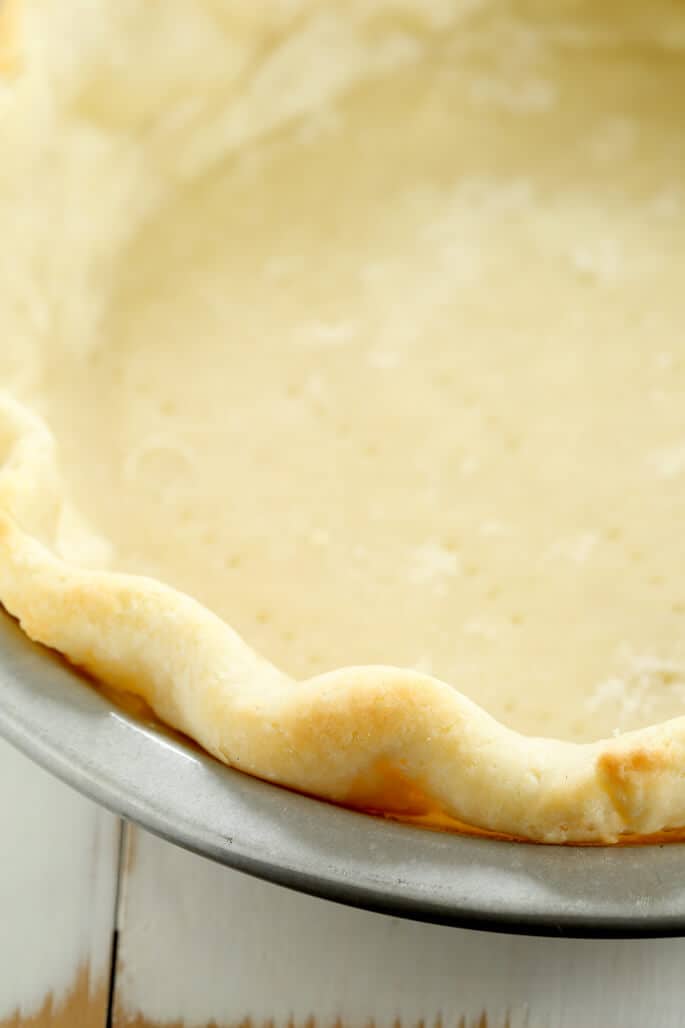 Closeup image of the crimped browned edge of pie crust in a metal pie plate