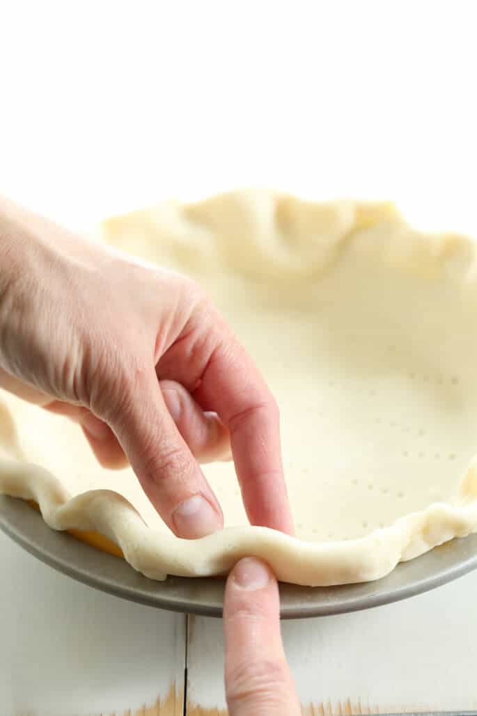 fingers crimping the edge of a raw pie crust in a metal pie plate