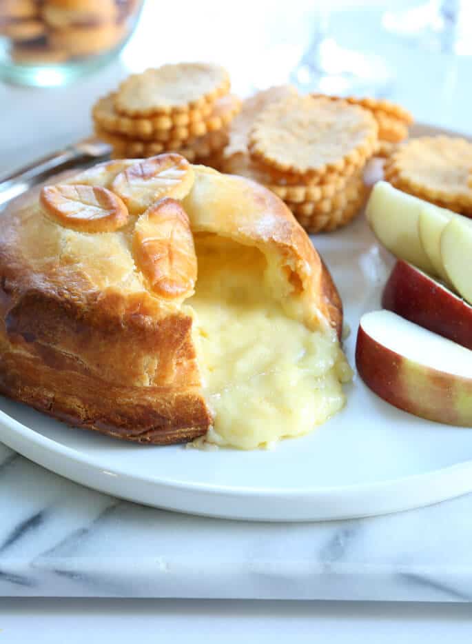 A white plate with Brie en Croute, apple slices and stacks of crackers 