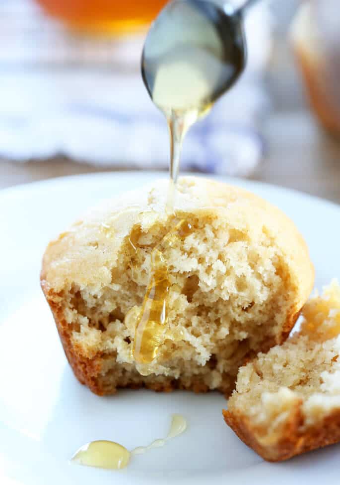 A close up of the inside of a light brown muffin on a white plate with honey on it