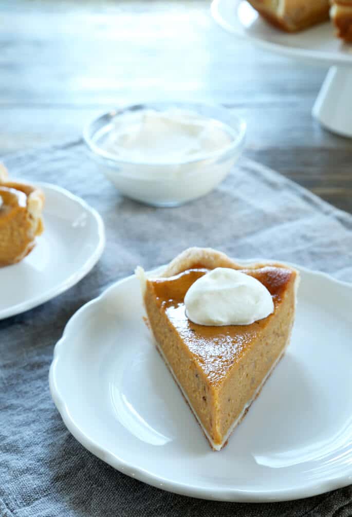 A slice of pumpkin pie with whip cream on a white plate