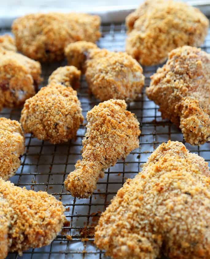 Browned and breaded baked chicken parts on a metal tray lined in parchment with a wire rack on top