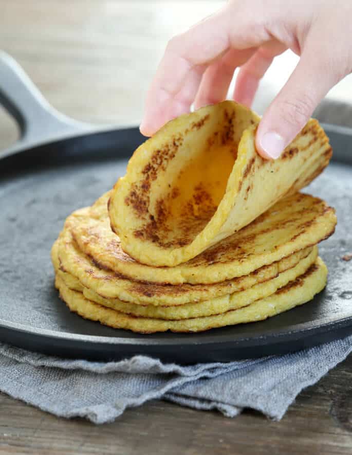 Cauliflower tortillas in a stack, a hand taking the top one.