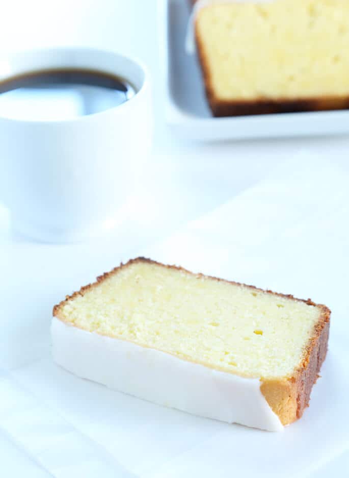 One slice of lemon pound cake on a small plate, with coffee.