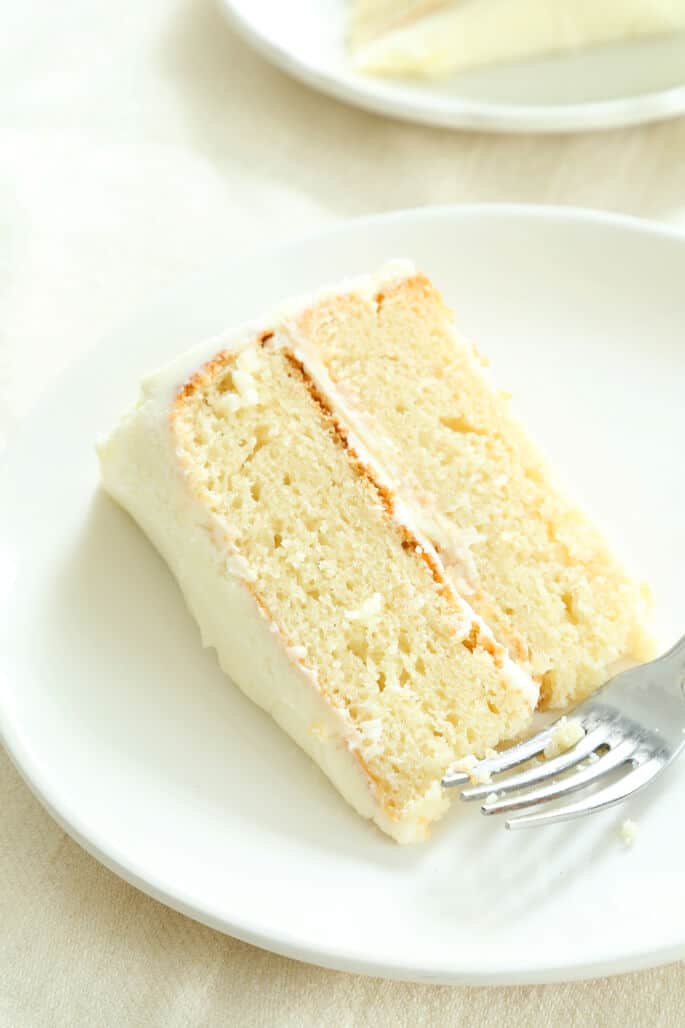 round white plate with slice of vanilla layer cake and a fork