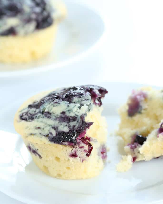 closeup image of broken light yellow muffin with blue swirl on top on small white plate