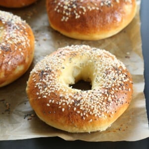 3 gluten free bagels with sesame seeds on brown paper on black baking sheet