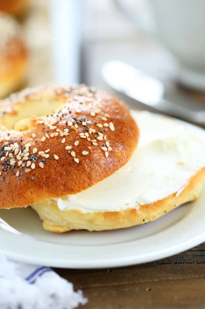 A close up of a bagel with seeds and cream cheese on white plate 