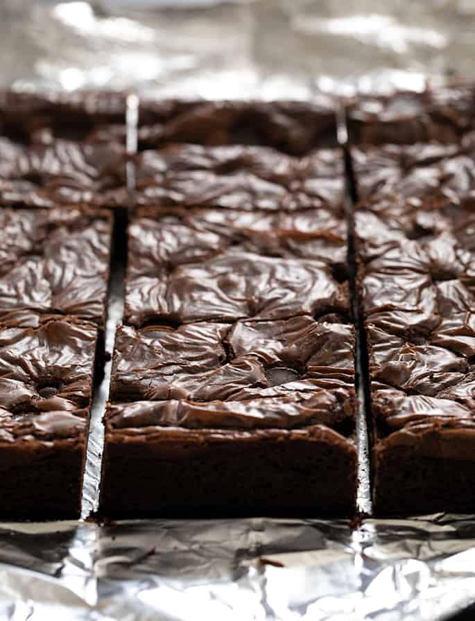 An image of sliced square flourless brownies on aluminum foil