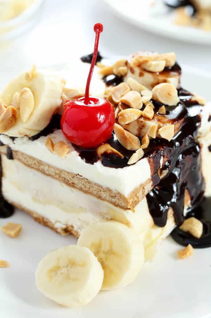 Close up of a banana spit cake with nuts, bananas and a cherry on a white surface