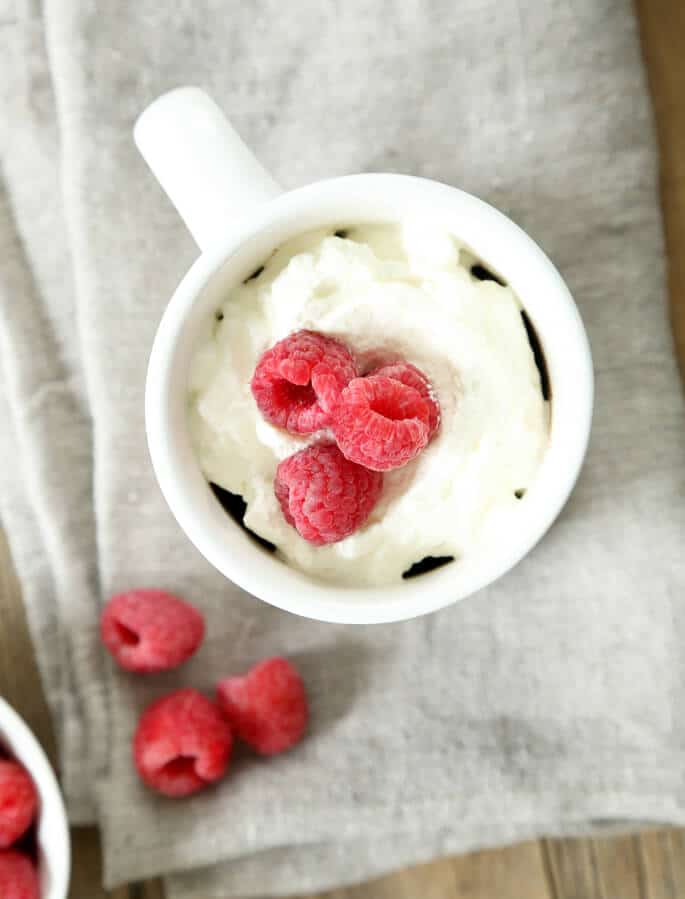 Overhead view of mug cake with whip cream and raspberries on a gray towel