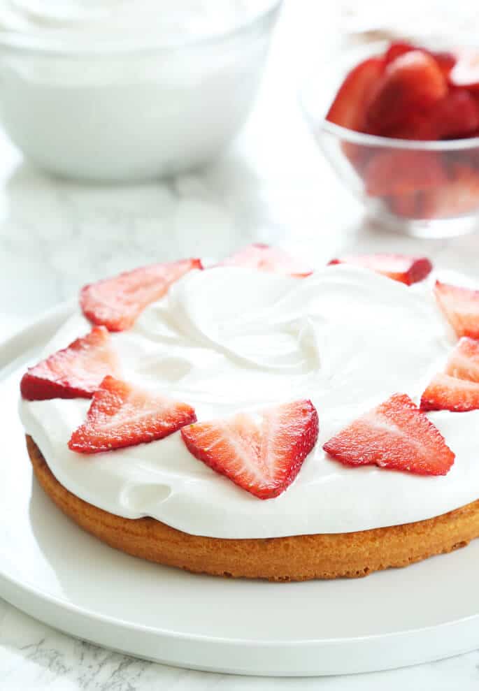 A sponge cake on a white cake with strawberries on top