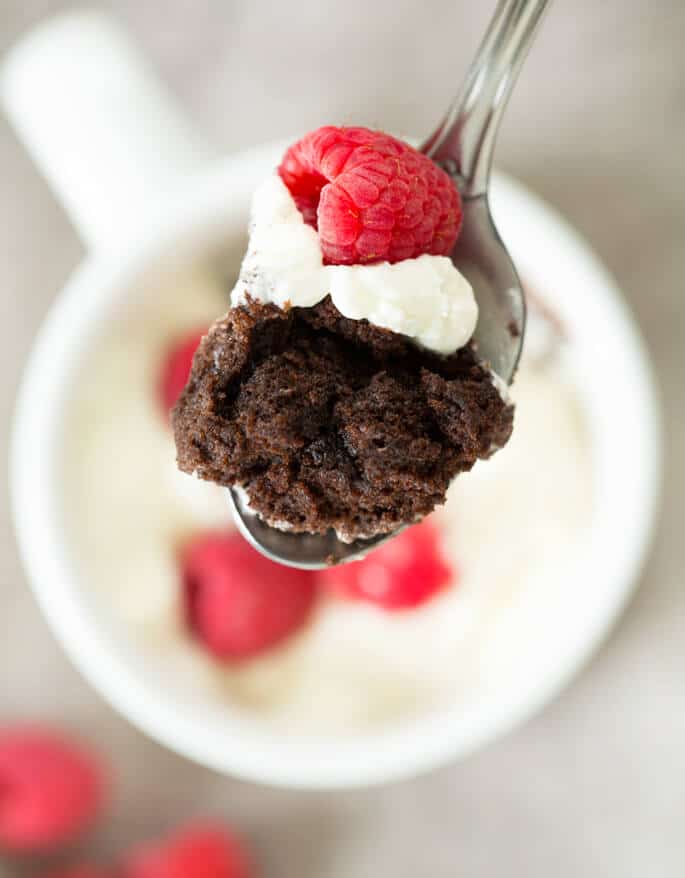 Close up of chocolate mug cake, whip cream and a raspberry on a spoon 