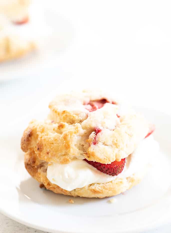 Lightly golden brown sliced in half strawberry biscuit with white whipped cream and sliced berries in the center