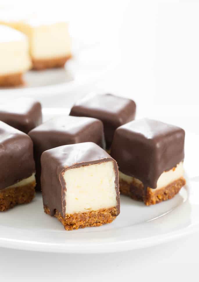 Cheesecake squares on a plate coated in chocolate, with one sliced open