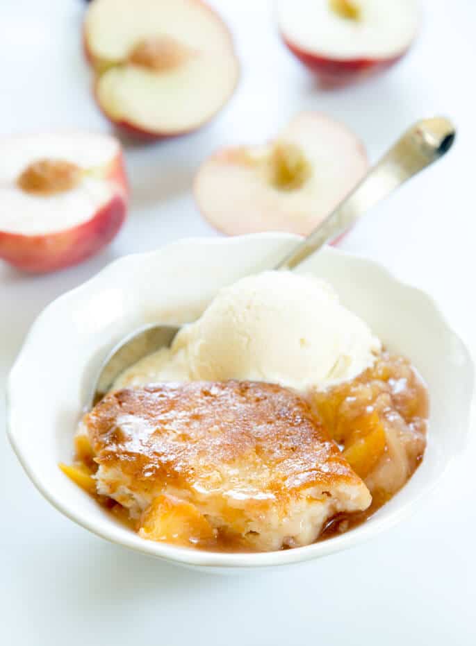 Close up of peach cobbler with a scoop of ice cream on white plate with metal spoon