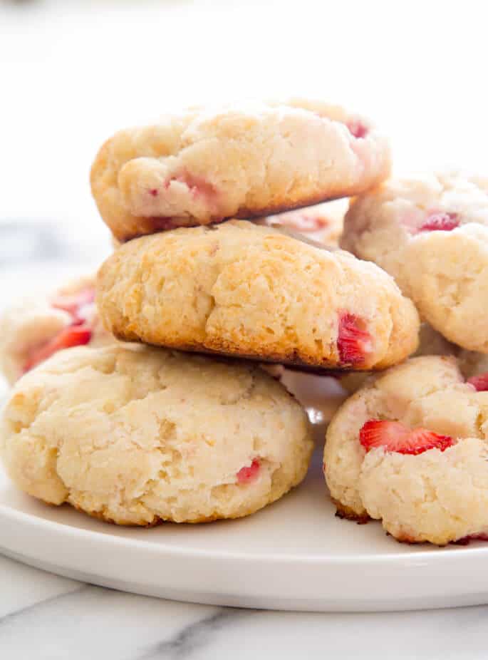 A white round serving platter with pale round biscuits with red strawberry pieces in a pile