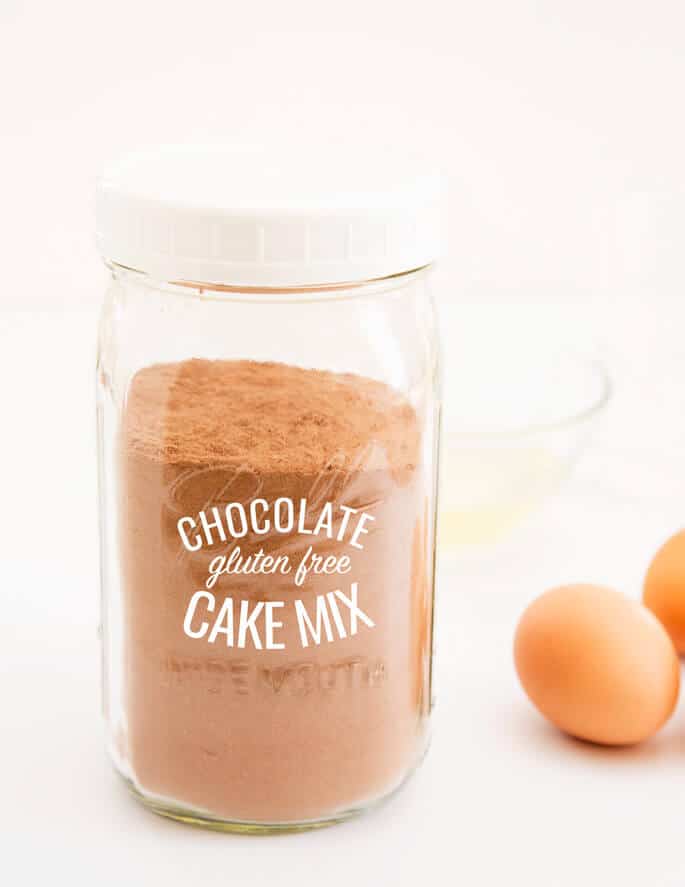 Chocolate cake mix in a jar with 2 eggs in back on white surface 