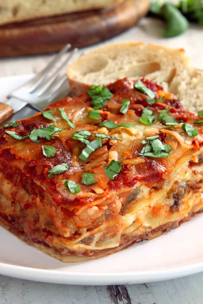 A close up side view of lasagna with herbs on top on a white plate