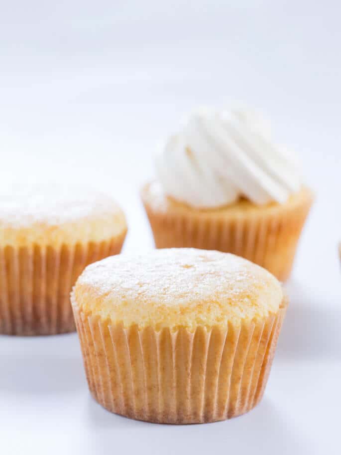 Close up of 3 vanilla cupcakes on white surface