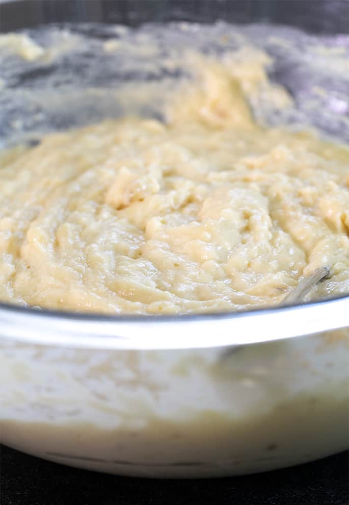 very pale brown/yellow soft glistening batter in glass mixing bowl with metal spoon peeking out