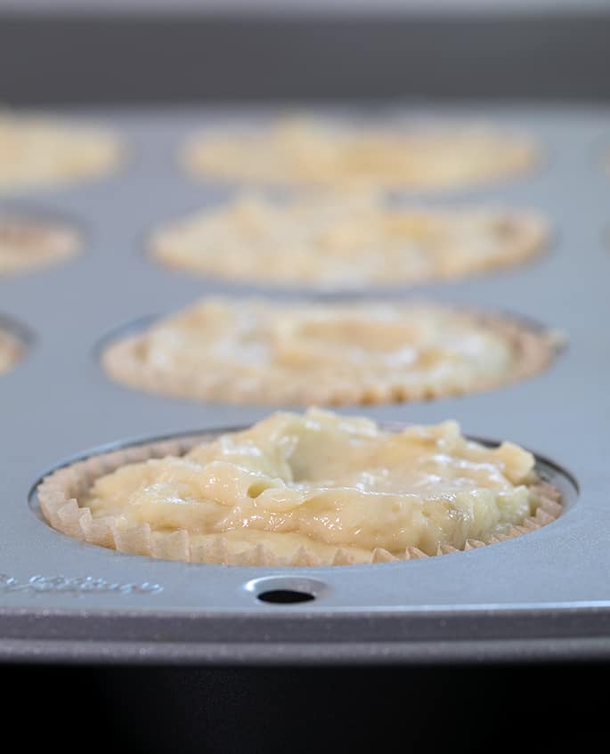 closeup image of light yellow/brown raw batter in metal muffin tin well with very light brown muffin tin liner