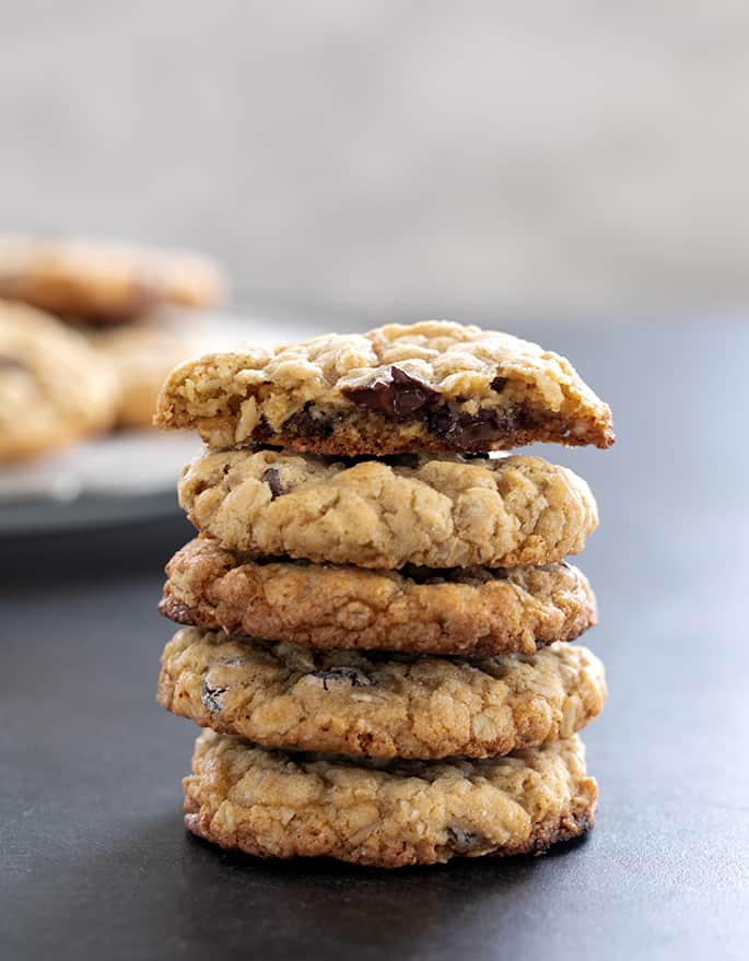 Stack of 5 crisp outside, chewy inside cookies with oats and chocolate chips with the top cookie broken in half