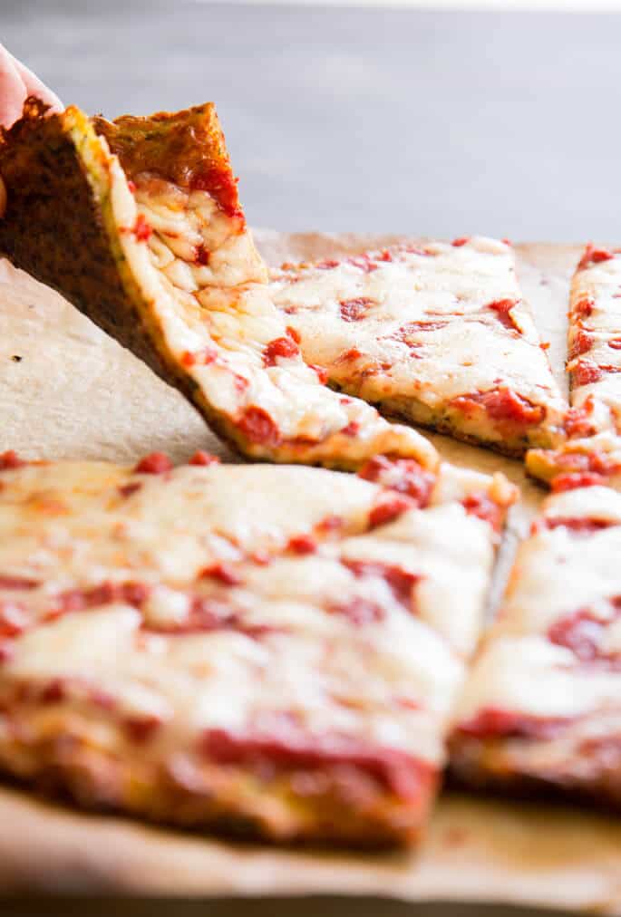 Zucchini pizza crust slices on brown paper with fingers folding one slice