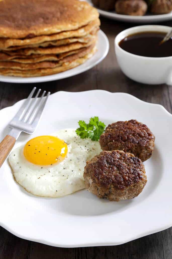 A white plate with a egg, 2 sausages and a fork 