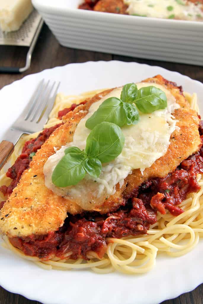 A close up of a spaghetti, red sauce and chicken parmesan on white plate