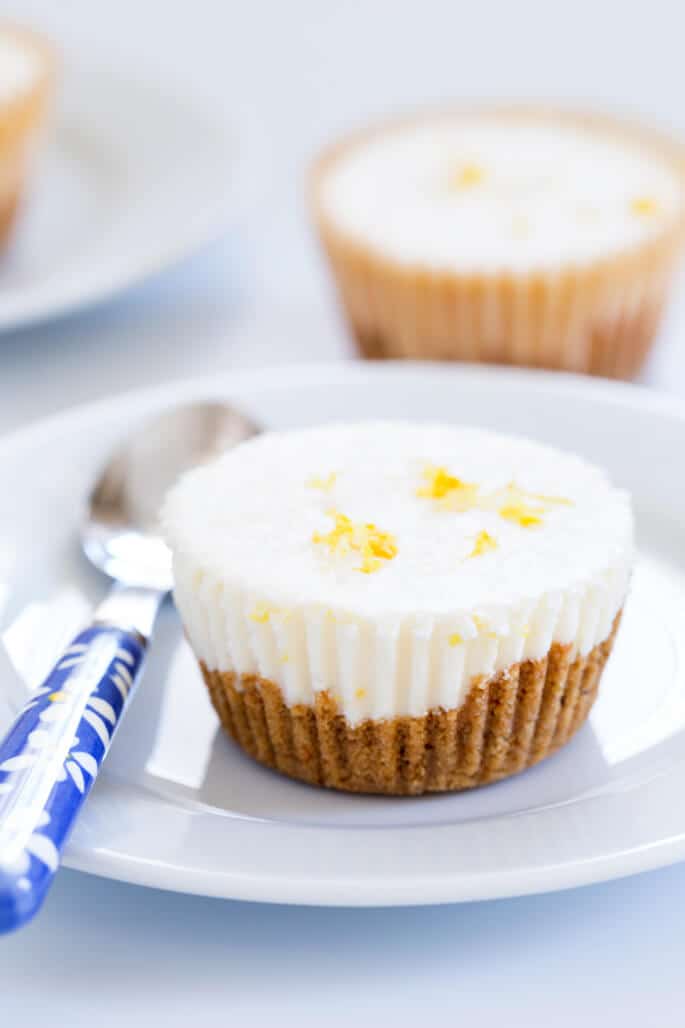 Clear side view of lemon cheesecake on white plate with blue spoon