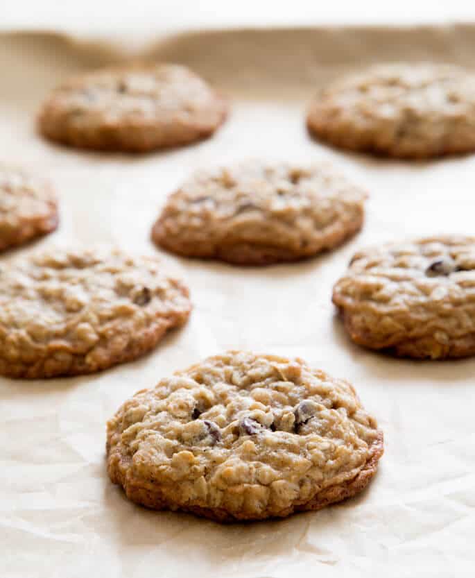 7 cookies just baked on a tray lined with brown paper with oats and chocolate chips