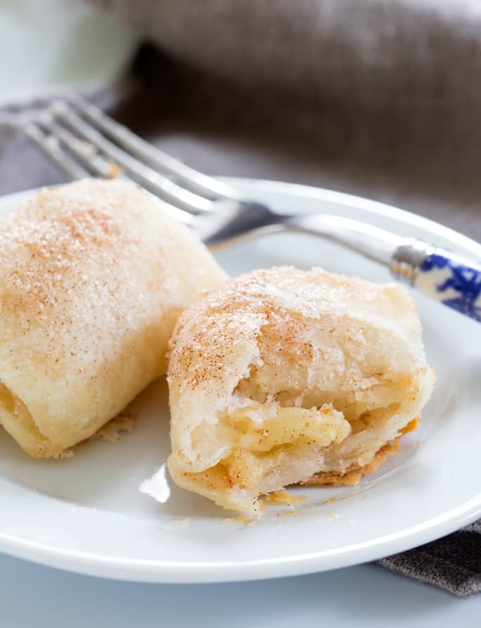 Close up of 2 apple dumplings in white plate with a blue fork