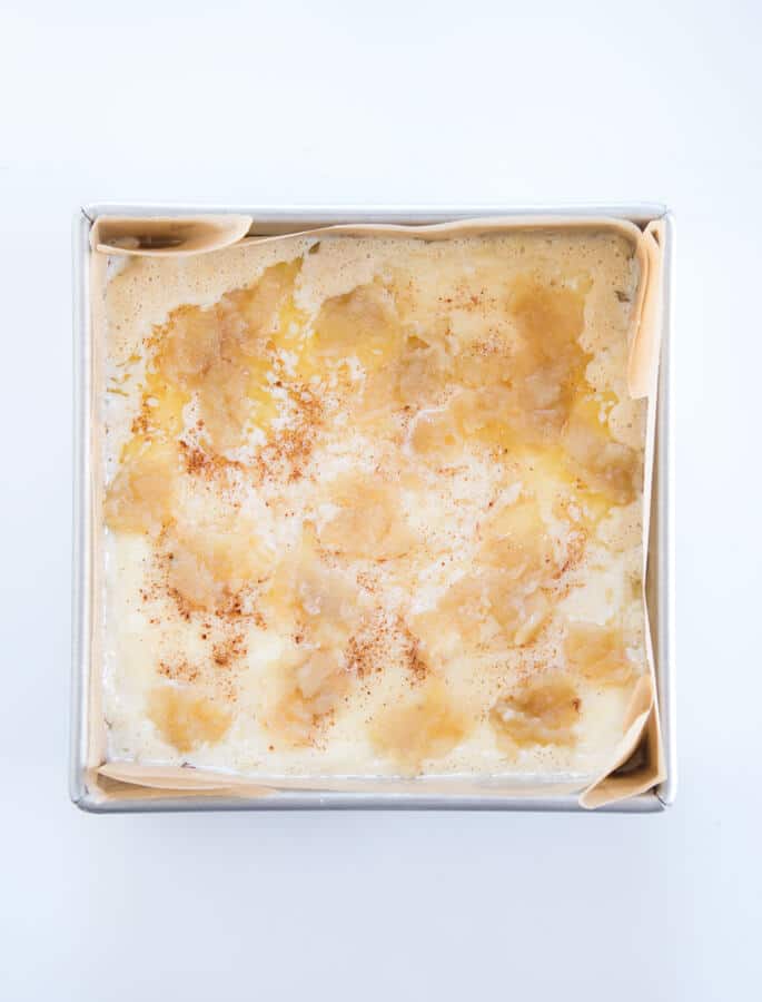 An overhead view of apple custard cake in metal tin on white surface 