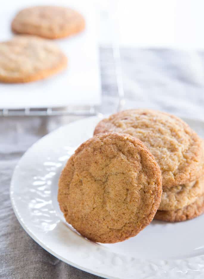 A stack of snickerdoodle cookies on a white plate with one cookie laying on the stack's side