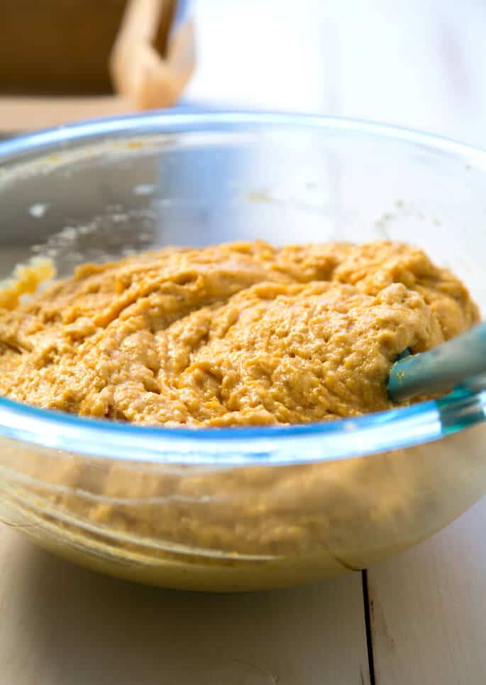 A bowl of pumpkin cornbread dough with a spatula 